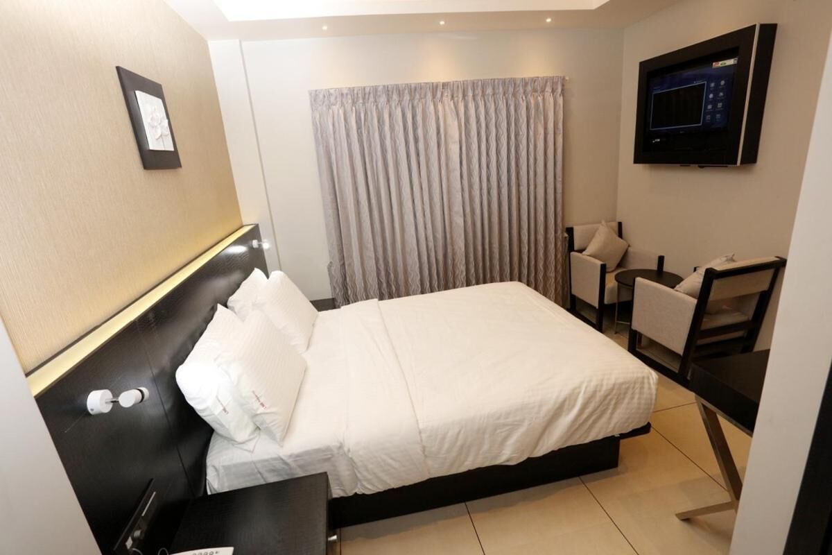 A hotel room with a bed, a desk, a chair, a TV, and a curtain.