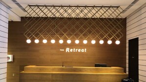 A reception desk with a wooden finish, two stools, and a wall-mounted light fixture. - THE Retreat (Iizuka)