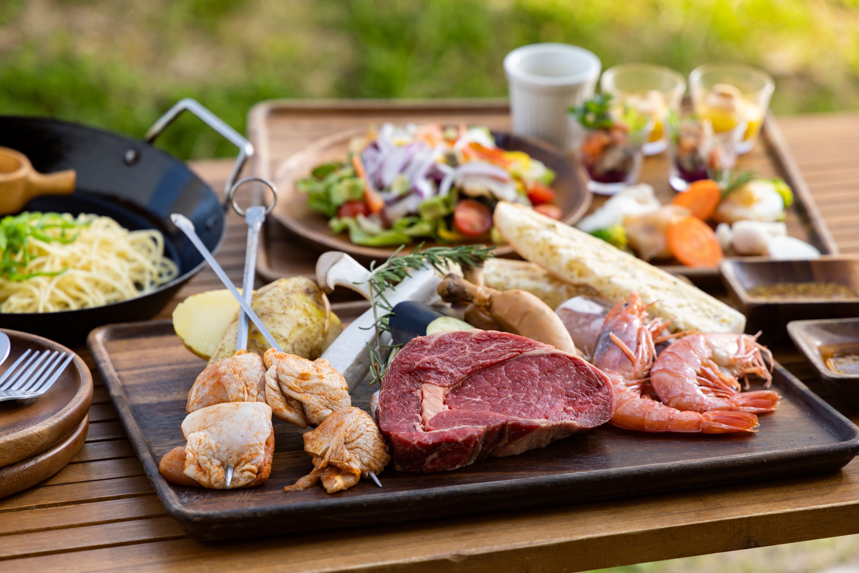 Una mesa de madera con una variedad de alimentos, como pollo a la parrilla, carne, camarones y verduras.