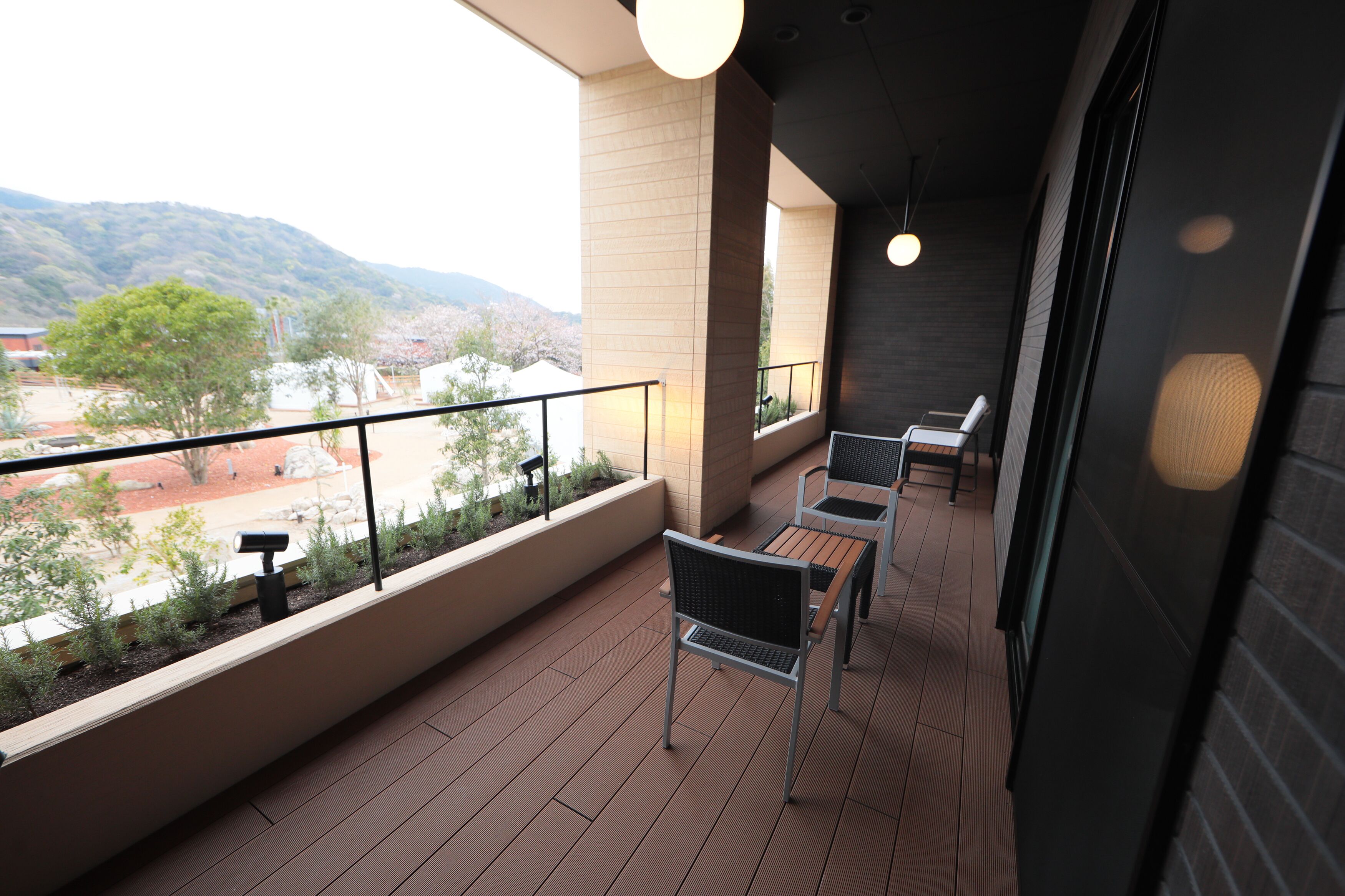 A balcony with a view of a hilly landscape, a railing, and a few chairs.