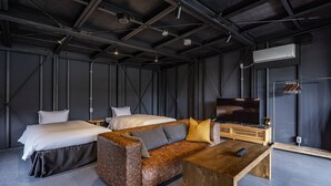 A modern hotel room with a bed, a sofa, a wooden coffee table, and a flat-screen TV. - THE Retreat (Iizuka)