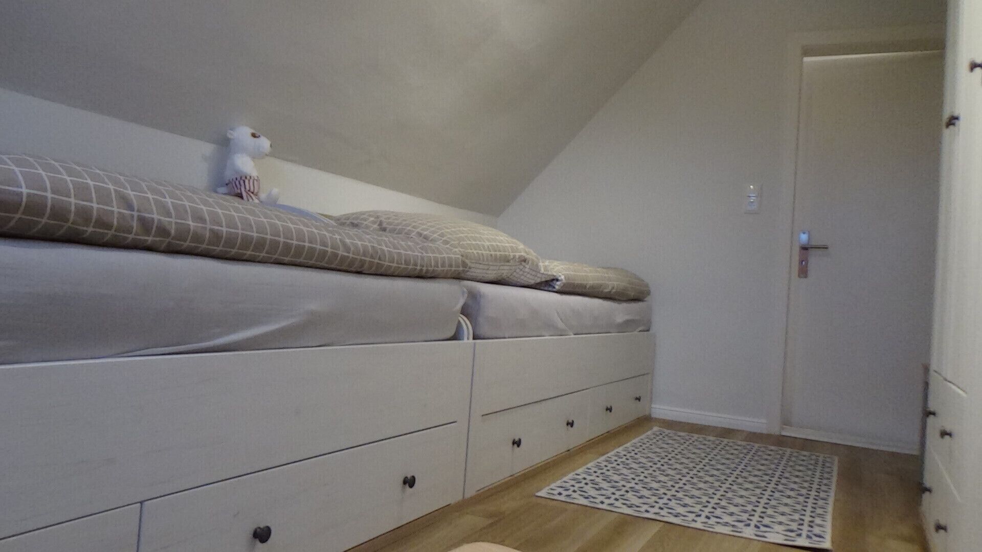 A bedroom with a bed, a dresser, a door, and a patterned rug.