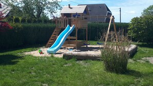 A wooden playhouse with a slide and stairs, surrounded by greenery and a clear sky. - Villa beach robber Rügen (Zudar)