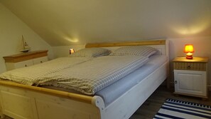 Una camera da letto con un letto in legno, due comodini con lampade, una piccola mensola con una nave in miniatura e un tappeto a righe.