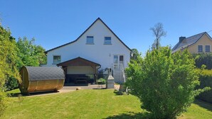 A two-story house with a sloped roof, a covered porch, and a large wooden barrel in the yard. - Villa beach robber Rügen (Zudar)