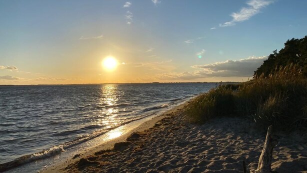 A beach with the sun setting over the water, a sandy shore, and some vegetation. - Villa beach robber Rügen (Zudar)