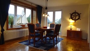 A dining area with a round table, four chairs, a ship's wheel decoration, and a lamp on a side table. - Villa beach robber Rügen (Zudar)