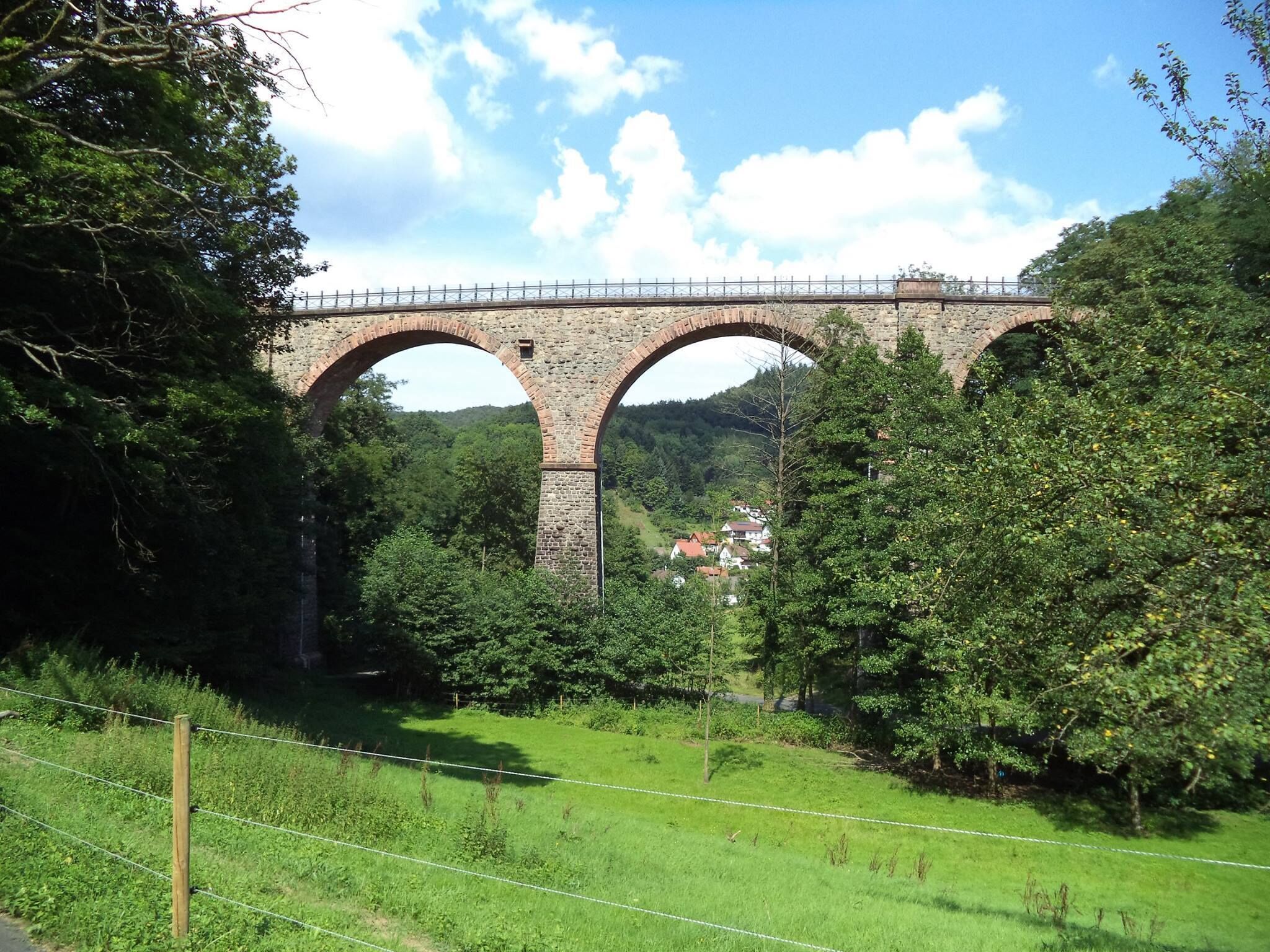 A stone bridge with three arches over a lush green landscape.