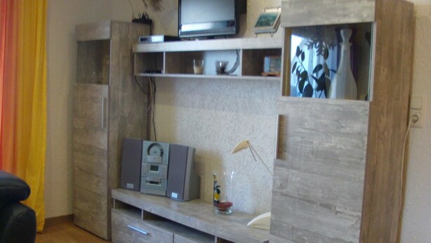 A living room with a wooden entertainment unit, a television, and a small cabinet.