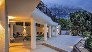 Un área de piscina moderna al aire libre con sillones de descanso y una escalera que lleva a un balcón.