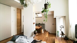 Ein modernes Wohnzimmer mit einer Couch, einem Couchtisch und einem Kamin. Hängende Pflanzen und ein Holzboden runden den Raum ab.
