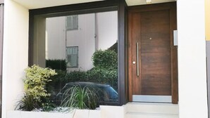 Ein moderner Eingangsbereich mit Holztür, weißer Wand und kleinem Garten mit Pflanzen.