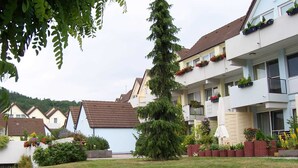 Ein Wohnhaus mit mehreren Balkonen, einem gepflegten Rasen und verschiedenen Kübelpflanzen.