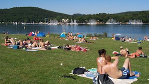 Ein Park am Seeufer, mit Menschen, die sich in der Sonne räkeln, Zelten und Booten im Wasser.