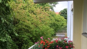 Ein kleiner Balkon mit rundem Tisch und Stühlen, umgeben von Blumentöpfen und Blumen.