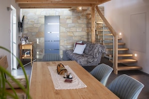A cozy living room with a stone wall, a wooden staircase, and a dining area with a table set for two.
