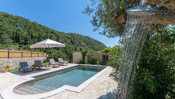 Una piscina con solárium de piedra, rodeada de sillas de descanso y una pérgola.