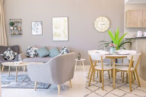 A modern living room with a grey sofa, a round dining table with chairs, and a clock on the wall. - Luton Vacation Homes Continental Tower (Dubai)