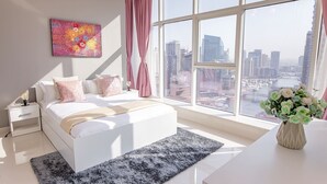 Une chambre moderne avec un grand lit, une table de chevet, une commode, une fenêtre donnant sur la ville et un tableau au mur.