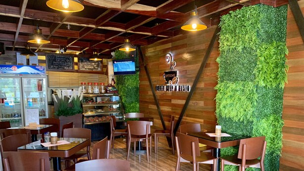 A café with wooden walls, green wall decorations, and a menu board. Tables and chairs are arranged for seating. - Davao Persimmon Suites (Davao)
