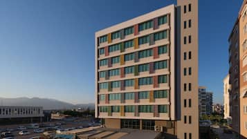 A multi-story hotel with a modern design, featuring a flat roof and a series of balconies with colorful awnings.