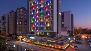 Un hotel de varios pisos con iluminación exterior de colores, un restaurante en la planta baja y un área de estacionamiento.