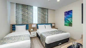 Habitación de hotel con dos camas, un ventanal grande, un cuadro y una mesita de noche con un teléfono y gafas.