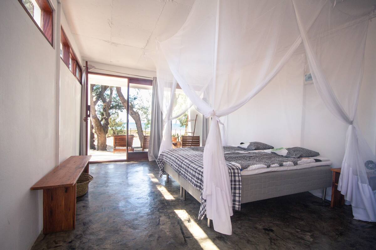 A bedroom with a bed, a bench, and a large window.