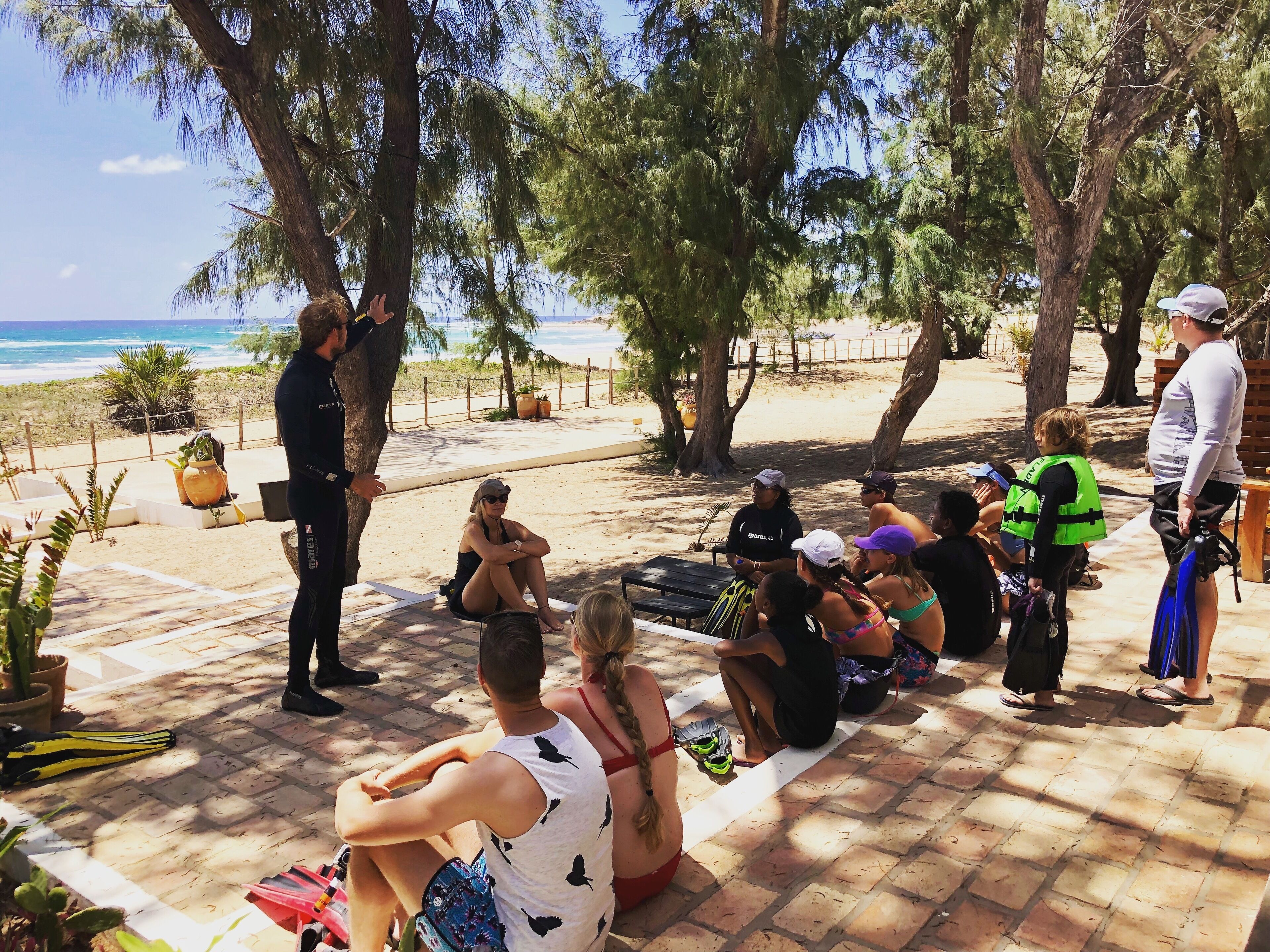 A group of people sitting and standing on a patio with a beach view.