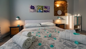 Un lit bien fait, avec des serviettes pliées, une tête de lit en bois et un mur en pierre qui attire l’attention.