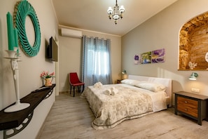 A bedroom with a bed, a TV, a red chair, a shower curtain, and a wall-mounted light fixture.