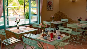Un café en plein air avec des tables et des chaises vertes, un mur en pierre et une vue sur la verdure.
