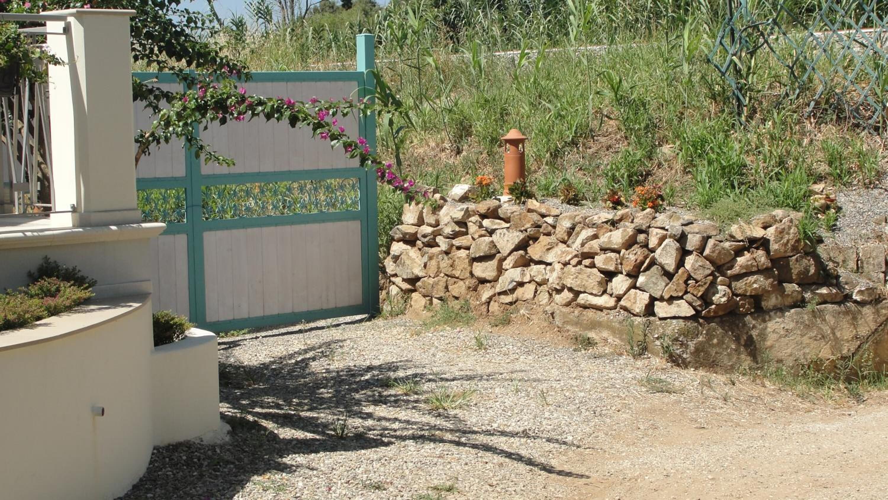 A stone wall with a gate, a small garden area with plants, and a clear sky.