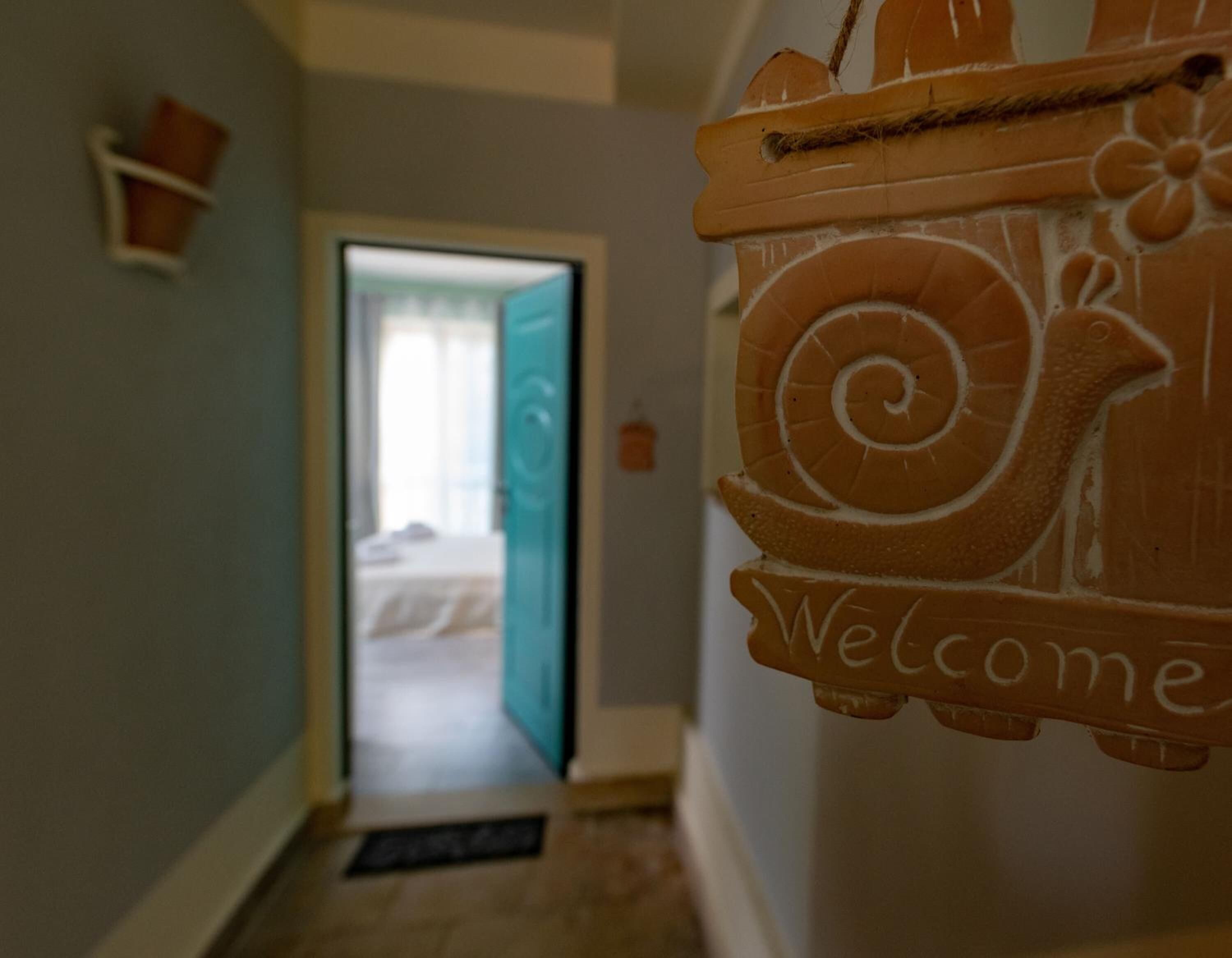 A hallway with a wooden welcome sign, a door leading to a room, and a small shelf with a container.