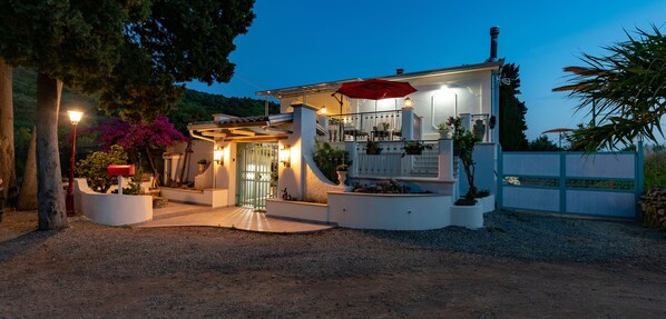 A two-story house with a covered porch, a red umbrella, and a gravel driveway.