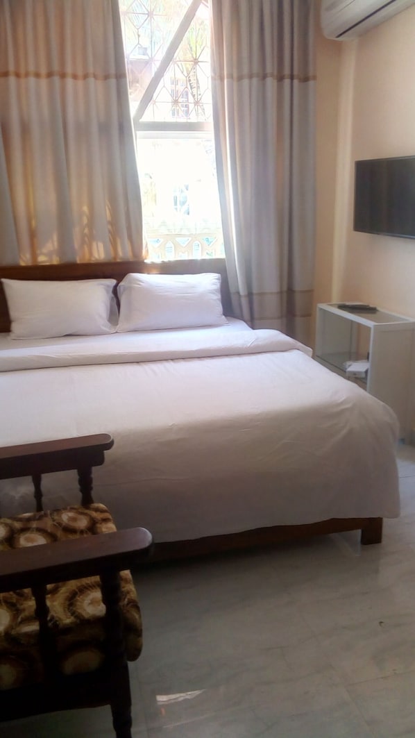 Une chambre d’hôtel avec un grand lit, une petite table, une chaise et un téléviseur fixé au mur.