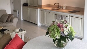 A modern kitchen with white cabinets, a sink, and a countertop. There is a dining area with a table and chairs, and a vase of flowers on the table.