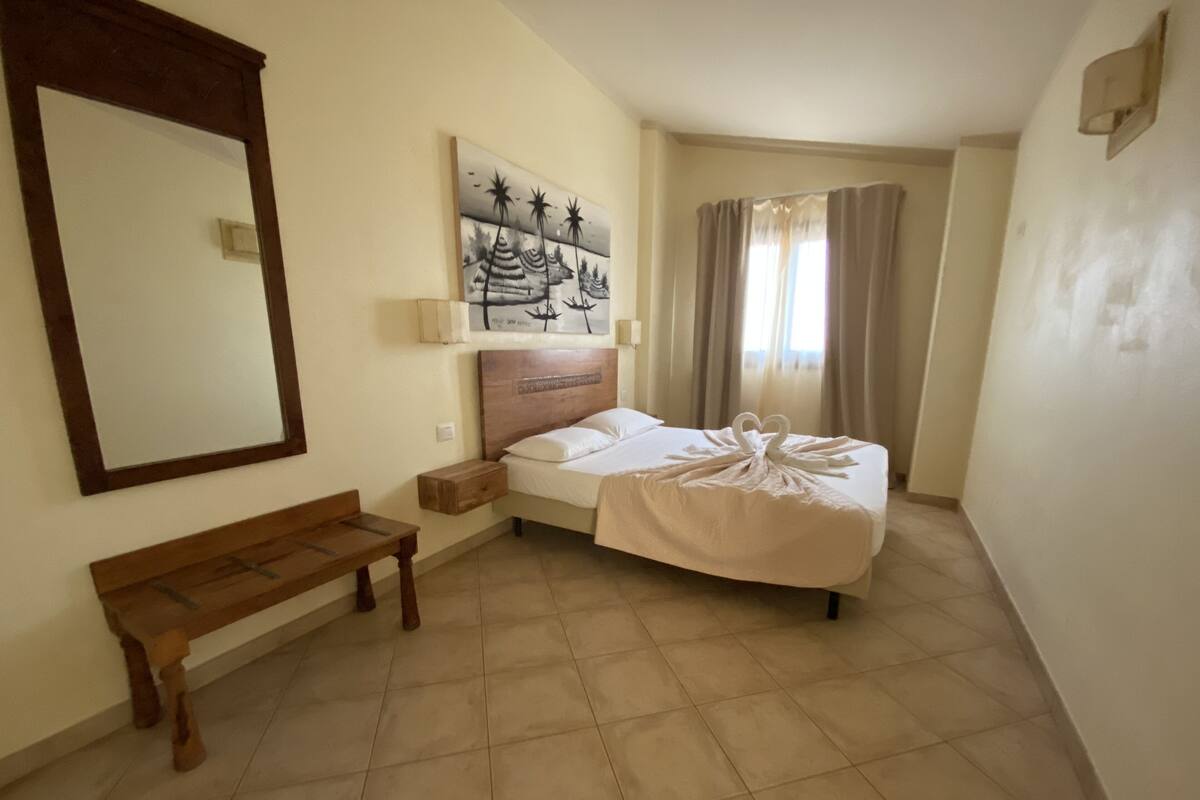 Een hotelkamer met een bed, een bankje, een schilderij en een grote spiegel.