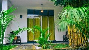 A modern building with a large glass door, surrounded by lush greenery and a small garden area. - Hotel Aram (Unawatuna)
