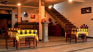 A hotel lobby with a staircase, a reception desk, and two tables with yellow checkered tablecloths. - Hotel Aram (Unawatuna)