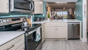 Una cocina moderna con electrodomésticos de acero inoxidable, gabinetes de color claro y una pared de acento color aguamarina.