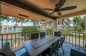 A balcony with a table and chairs, overlooking a pool and palm trees.