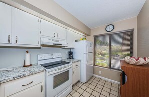 A compact kitchen with white cabinets, a stove, a refrigerator, and a clock on the wall. - Waterfront 2BR/2BA Isla Del Sol condo with pool, hot tub, balcony, and views. (St Petersburg)