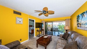A living room with yellow walls, a ceiling fan, a sofa, a coffee table, and a view of a balcony. - Waterfront 2BR/2BA Isla Del Sol condo with pool, hot tub, balcony, and views. (St Petersburg)