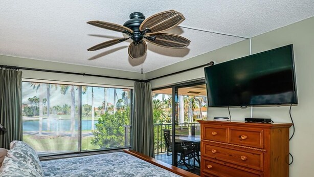 A hotel room with a bed, a wooden dresser, a television, and a ceiling fan. - Waterfront 2BR/2BA Isla Del Sol condo with pool, hot tub, balcony, and views. (St Petersburg)