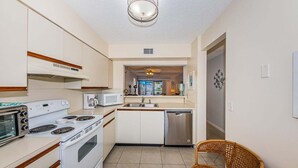 Una cucina compatta con piano cottura, microonde e lavastoviglie, una zona pranzo con tavolo e sedie, e vista sull'area soggiorno.