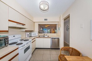 Una cocina compacta con estufa, microondas y lavavajillas, un comedor con mesa y sillas, y vista al área de estar.