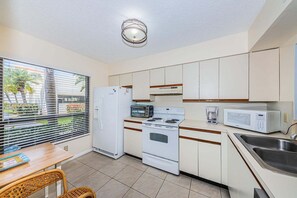 A compact kitchen with white appliances, a dining area with a table and chairs, and a window with blinds.