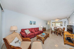 A living room with a red sofa, beige armchairs, a coffee table, and a dining area with wooden chairs and a table.