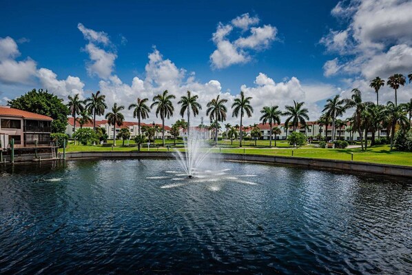 A fountain in a courtyard with palm trees and buildings in the background.